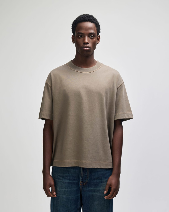 A heavyweight cotton unisex boxy t-shirt in khaki, displayed on a model with dark jeans. It features a logo.