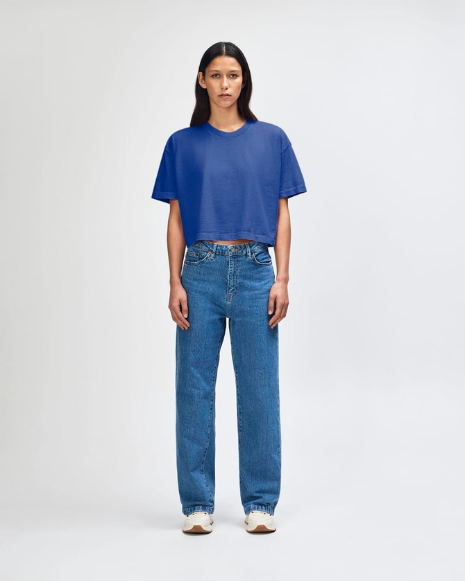 A blue crop boxy T-shirt worn with high-waisted blue jeans. The model stands against a plain background.