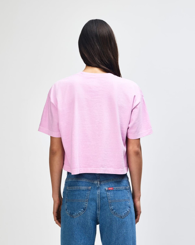 A back view of a pink cropped boxy t-shirt made from heavyweight cotton, worn with blue jeans. Features a logo.