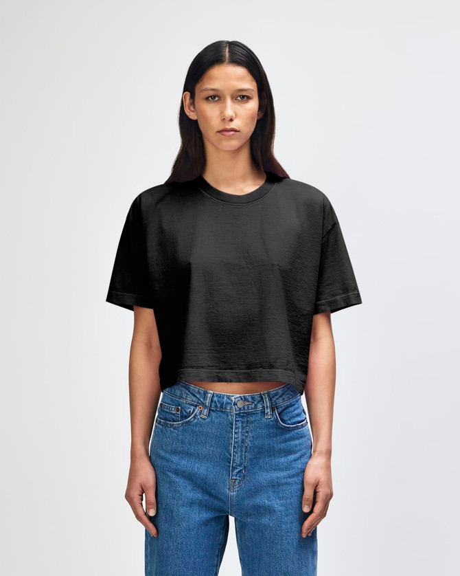 A black heavyweight cotton women's crop boxy t-shirt on a model, paired with blue jeans. It features a logo.