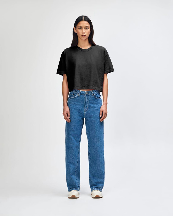 A black crop boxy T-shirt paired with blue straight-leg jeans, modelled by a standing woman. The outfit features a logo.