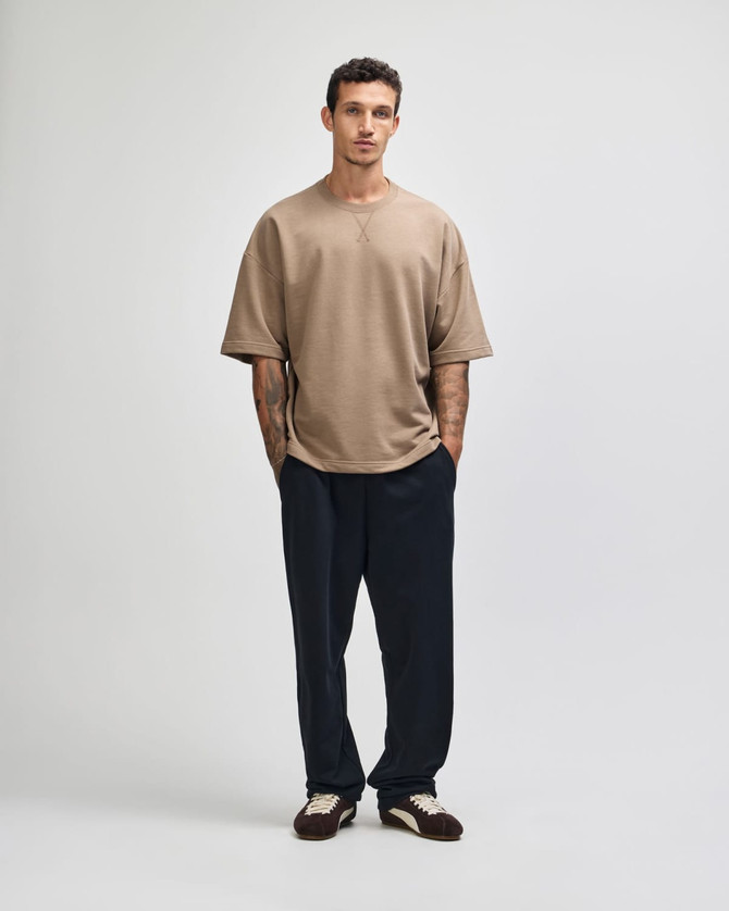 A model wearing a beige oversized boxy top and dark blue pants, standing against a neutral background.