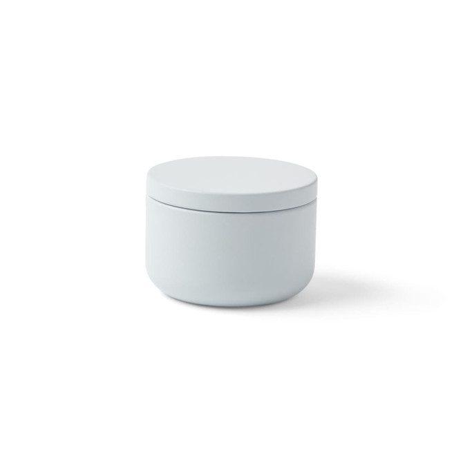 A mini tin candle in a soft grey container with a smooth lid. The container has a round shape.