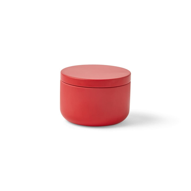 A red mini tin candle with a smooth, rounded design and a flat lid. The tin has a simple, modern aesthetic.