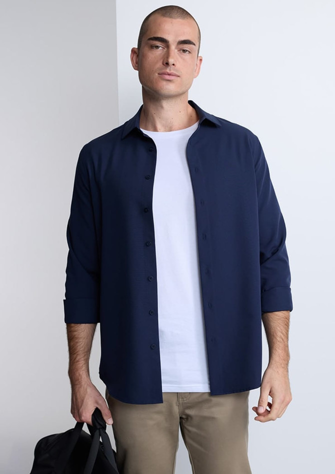 A man wearing a navy long sleeve shirt over a white t-shirt, holding a black bag. The shirt features button details.