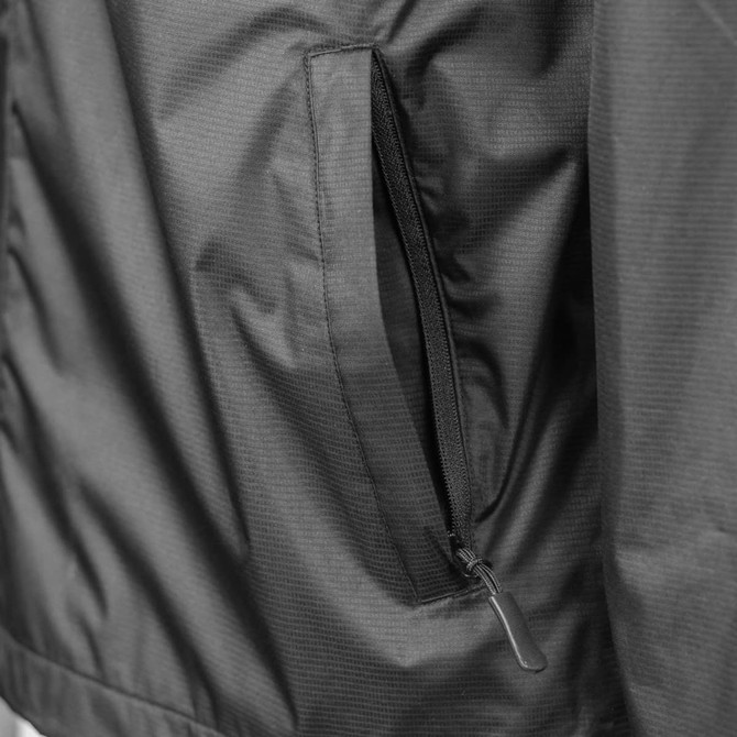 A close-up of a black TRENDSWEAR Wellington Unisex Windbreaker featuring a zippered pocket and soft shell fabric.