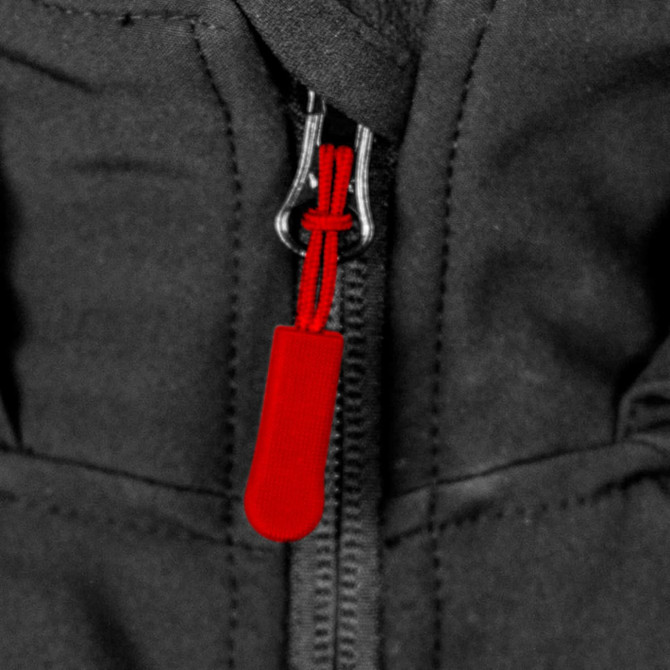 A close-up of a black soft shell jacket featuring a red zipper pull and a logo.