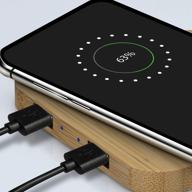 A bamboo wireless charging hub with a smartphone displaying charging status. The hub has two connected cables.
