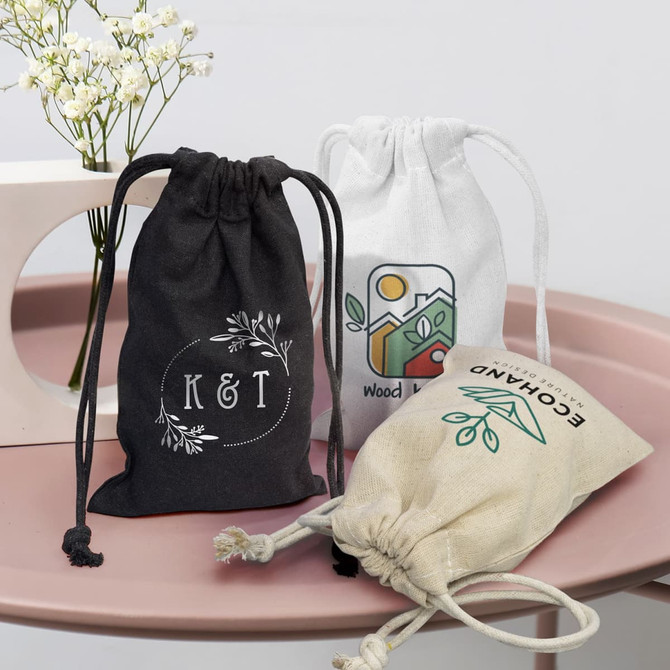 Three small cotton gift bags in black, white, and natural colour, featuring various designs and drawstring closures.