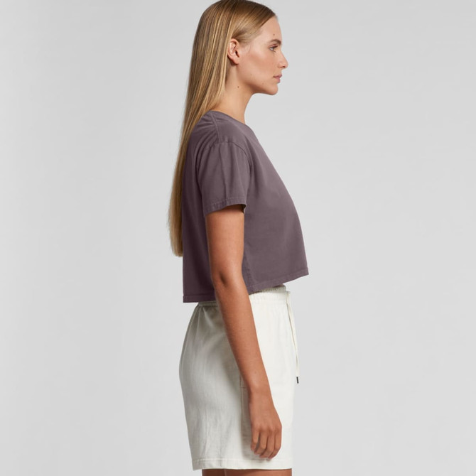 A cropped t-shirt in a muted purple shade, modelled by a woman standing sideways, paired with light-coloured shorts.