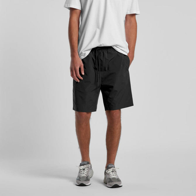 Black sports shorts with an elastic waistband, modelled by a person wearing a white t-shirt and grey sneakers.