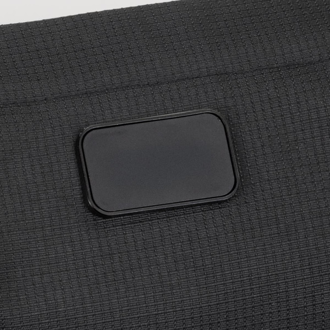 A close-up of a textured black sling bag featuring a rectangular logo patch.