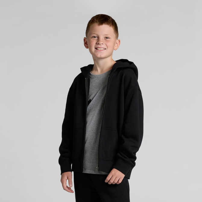 A young boy stands wearing a black Youth Relax Zip Hood hoodie over a grey t-shirt. The hoodie has a front zip and a hood.
