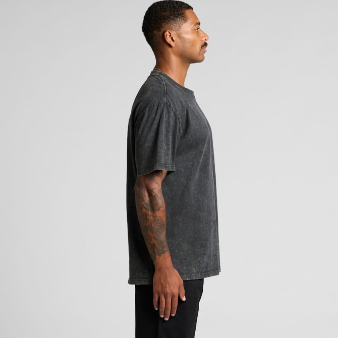 A man stands in profile wearing a dark stone wash heavy T-shirt. The shirt has a relaxed fit and visible texture.