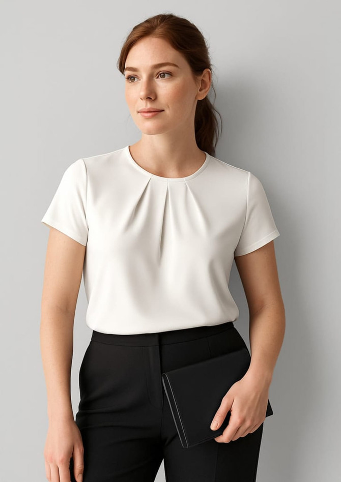 A woman wears a white short sleeve top with a pleat design, paired with black trousers and holding a clutch.
