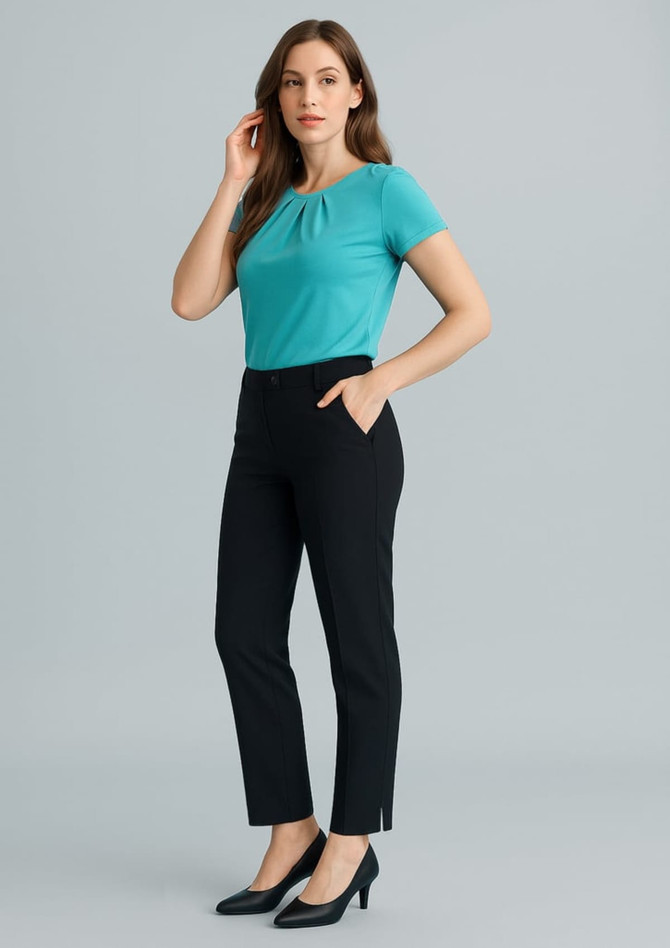 A woman wearing a turquoise top and black slim leg pants, standing against a light grey backdrop. The pants feature pockets and a logo.
