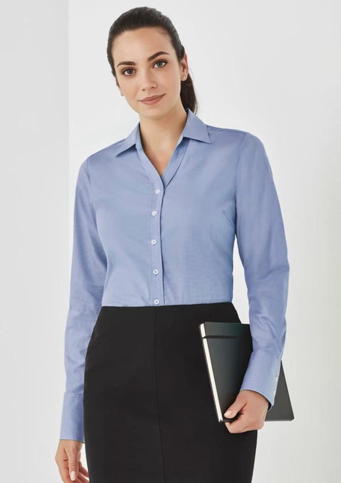 A woman in a light blue button-up long sleeve shirt holds a tablet, set against a neutral background.