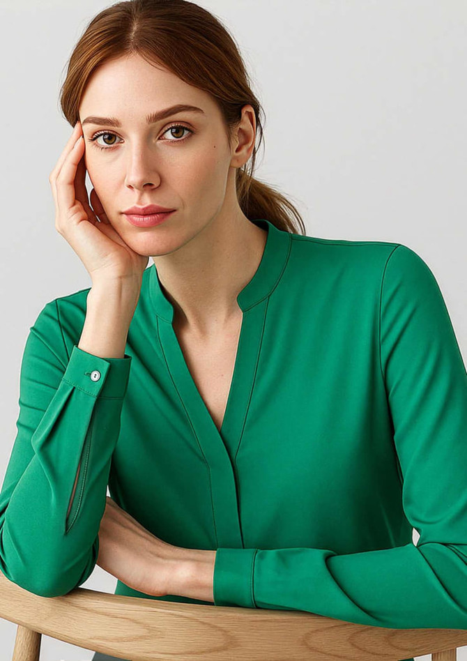 A green long sleeve blouse with a V-neck design, featuring button details on the sleeves. The model poses thoughtfully.