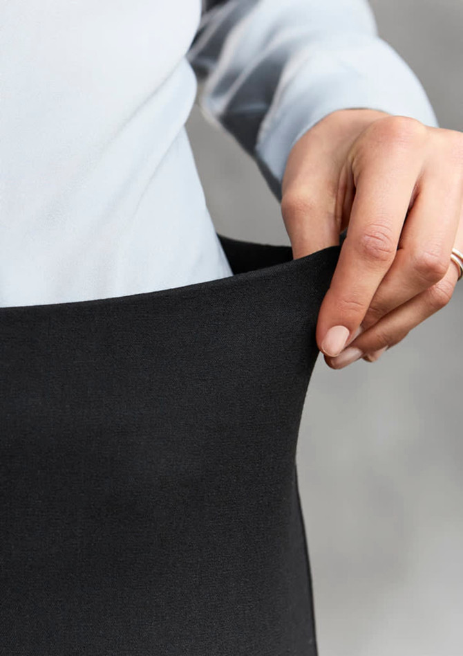 A hand holding the waistband of black women's leggings with a grey background. The leggings feature a smooth texture.