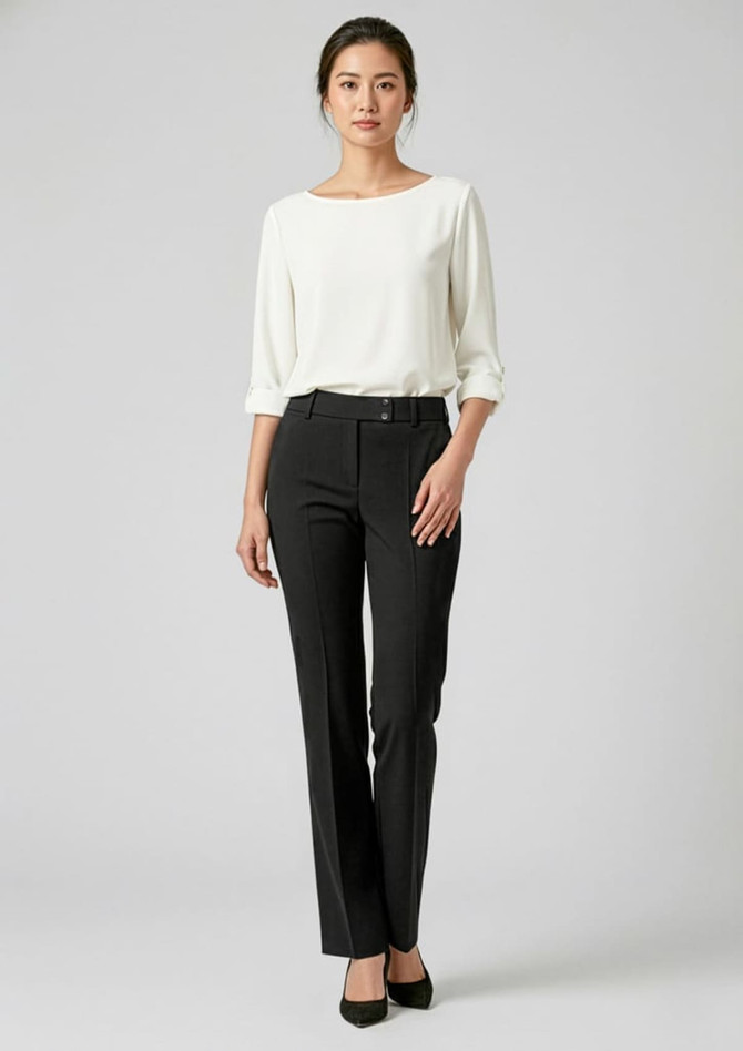A woman stands in sleek black slacks paired with a light-coloured top and heels, showcasing a stylish look.