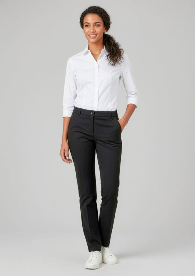 A woman in a fitted white shirt and black straight-leg pants stands smiling with a hand in her pocket.