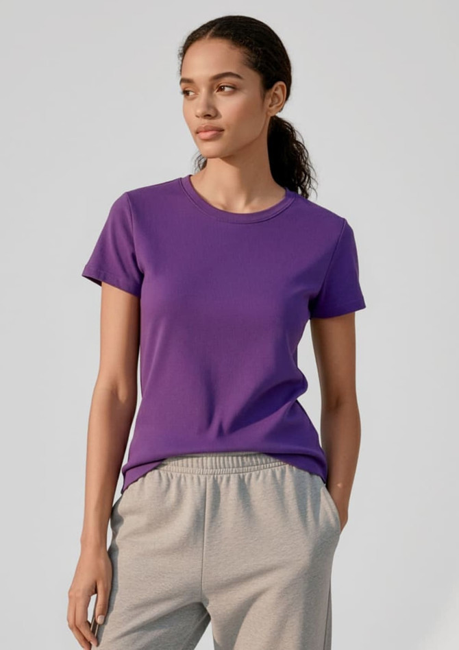 A purple women's short sleeve tee displayed on a model, paired with grey pants. The tee features a simple design and branding.