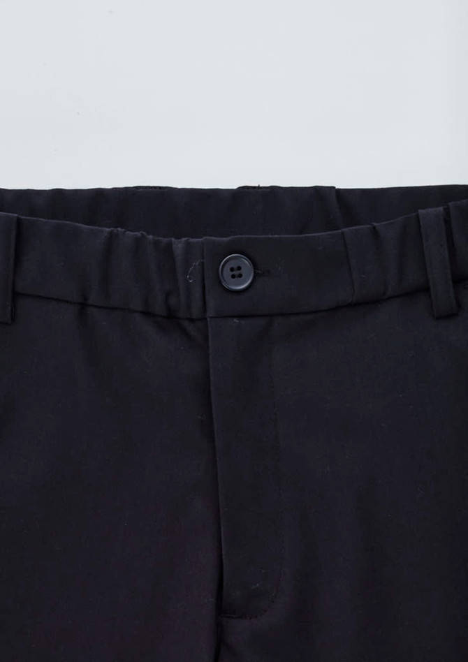 A close-up of black cargo pants featuring a button closure and elastic waistband. Logo present.