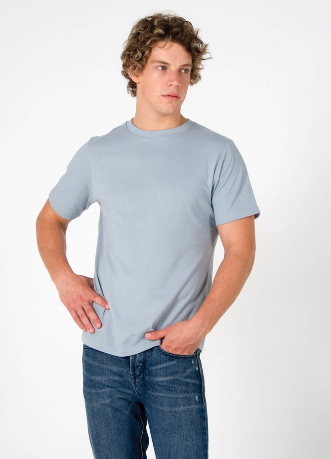 A light blue men's slim fit T-shirt displayed, paired with denim jeans. The shirt has a simple design and a logo.