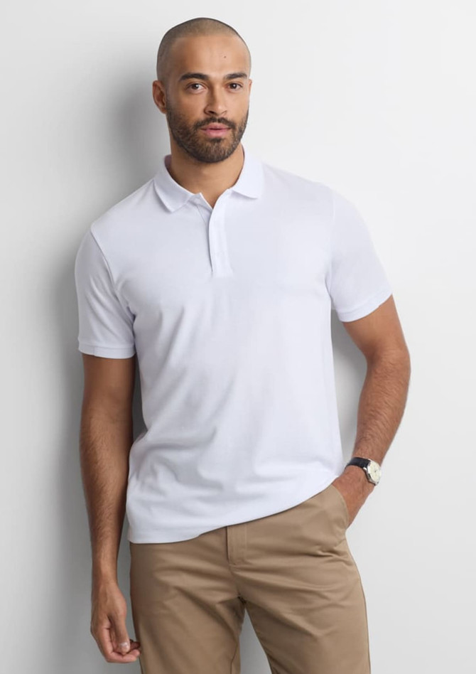 A white short sleeve polo shirt with a collar, worn by a man standing against a light background.
