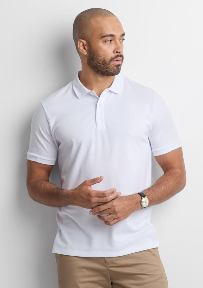 A white short sleeve polo shirt is worn by a man standing against a neutral background, featuring a subtle logo.