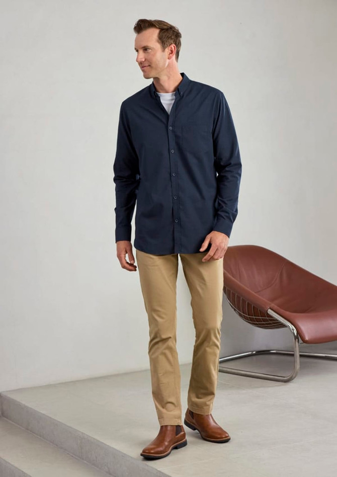 A long sleeve button-up shirt in navy, paired with beige trousers and brown boots, displayed in a minimalist setting.