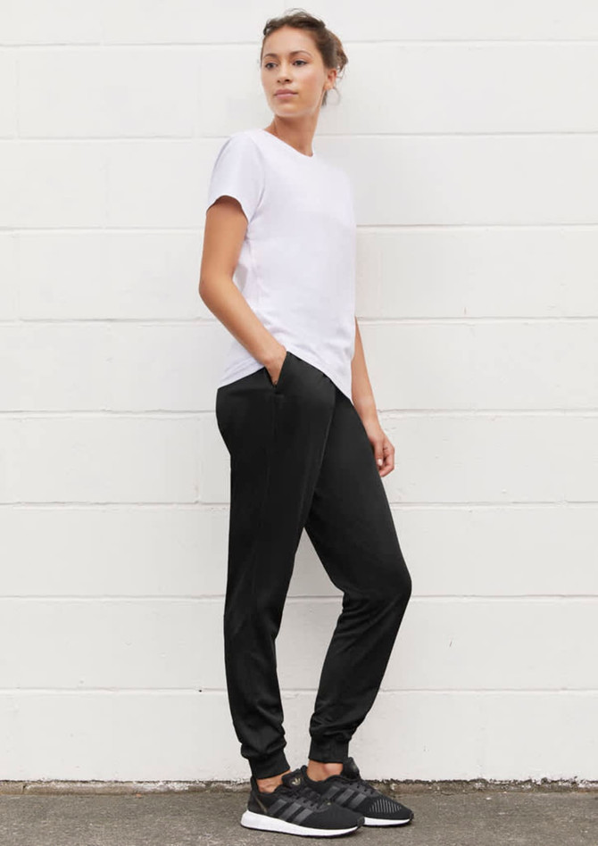 A woman stands in profile wearing a white t-shirt and black track pants with pockets, complemented by black sneakers.