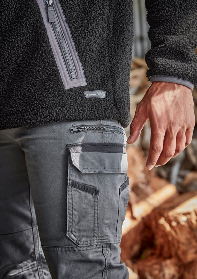 A close-up of men's grey work pants featuring multiple pockets and a zipped side pocket, paired with a black fleece top.