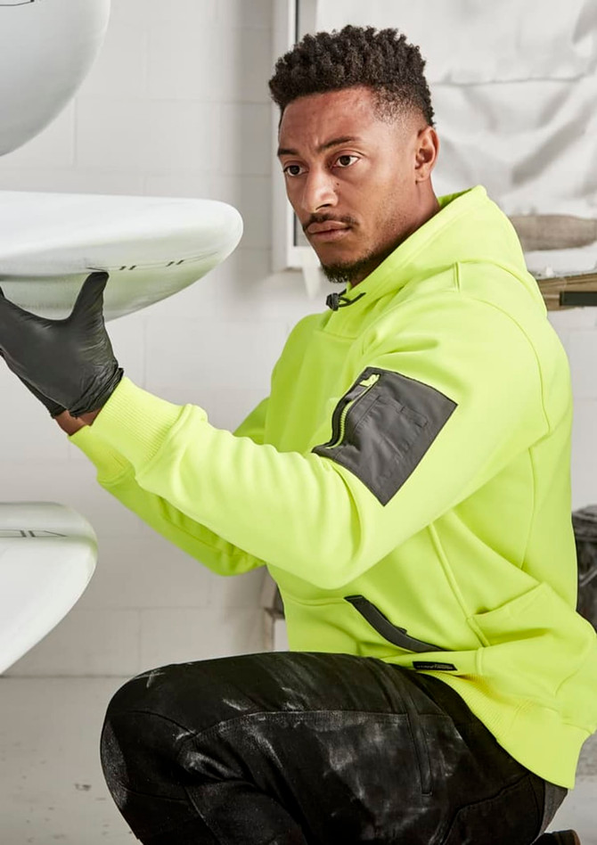 A bright yellow unisex water-resistant hoodie with black detailing, featuring a logo, worn by a person working on surfboards.