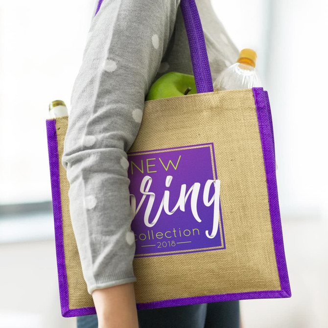 A jute tote bag in natural and purple, carried with a drink bottle and an apple visible inside.