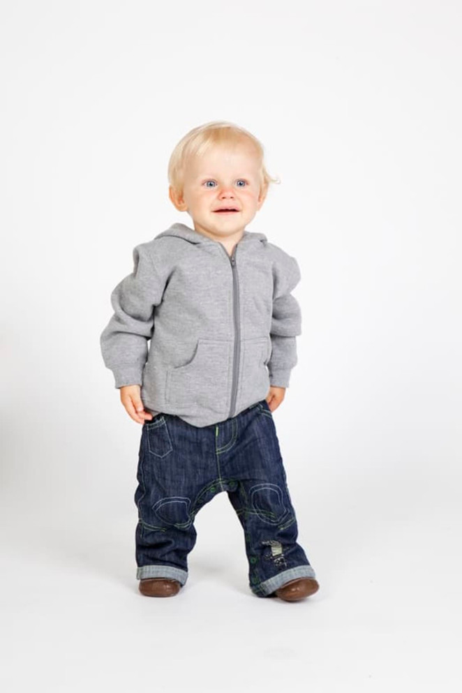 A grey fleece baby zip hoodie worn by a toddler, paired with blue denim jeans. The child is smiling and standing.
