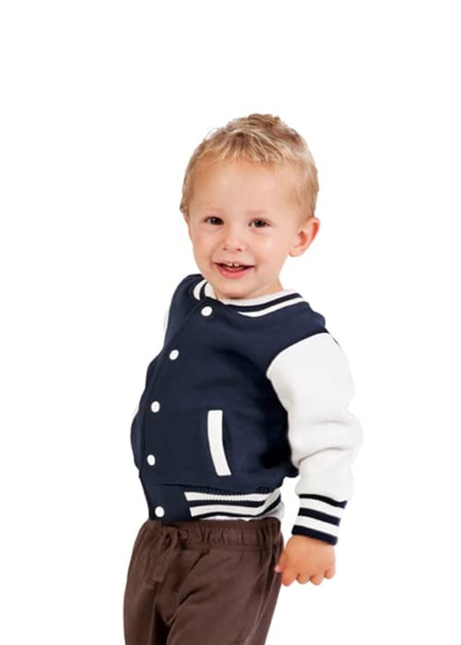 A baby wearing a navy and white varsity jacket, smiling and standing against a white background.