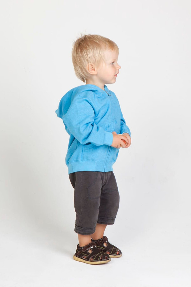 A light blue zip hoodie for babies, paired with dark grey shorts and sandals, displayed on a child standing sideways.