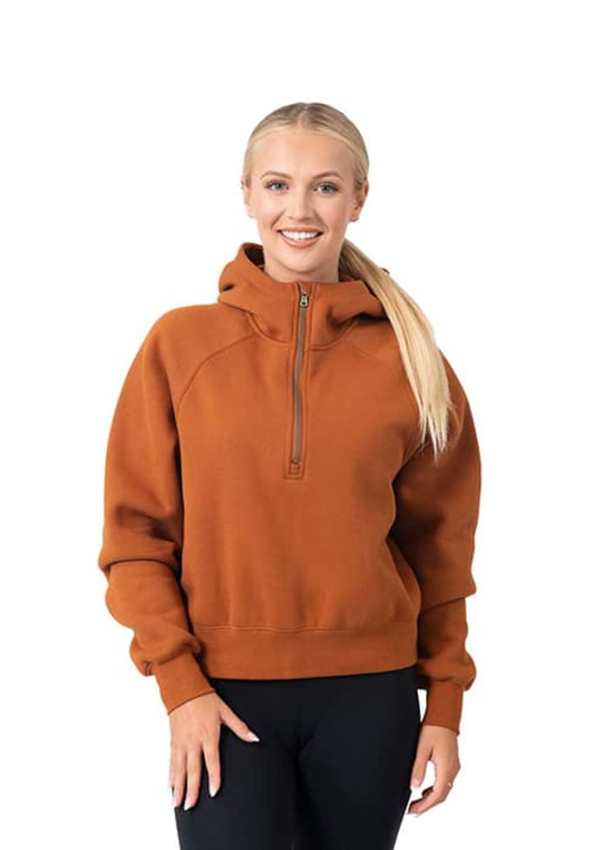 A woman wearing a rust-coloured half-zip jumper with a hood, featuring a slight relaxed fit and long sleeves.