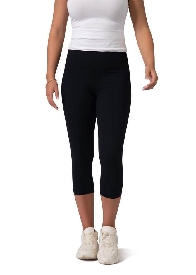 Black high-rise 3/4 leggings worn with a white tank top and white sneakers, featuring a logo on the waistband.