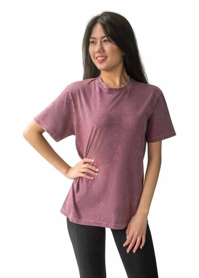 A model wearing a unisex stone wash T-shirt in a burgundy colour, paired with black leggings. The shirt has a logo.