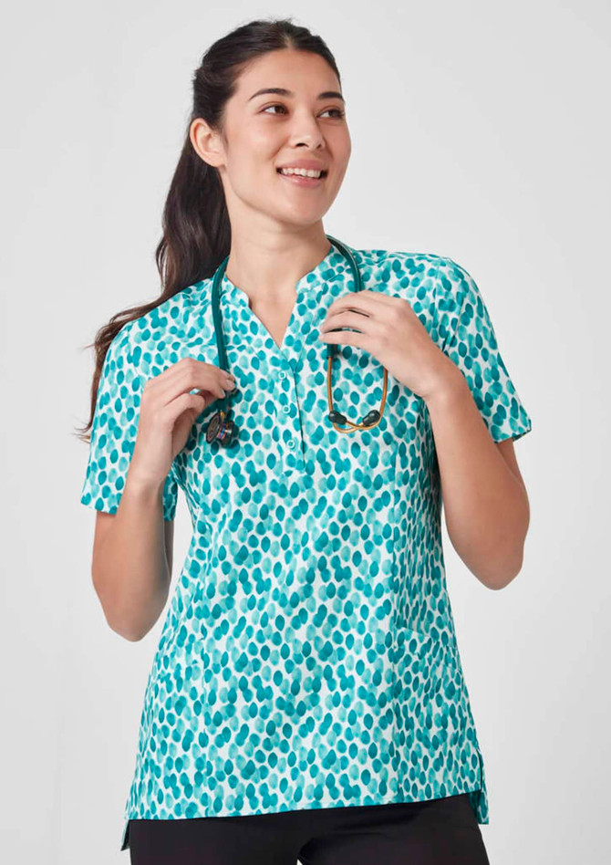 A turquoise tunic with a stardust print, featuring a collar and short sleeves, worn by a smiling woman holding a stethoscope.