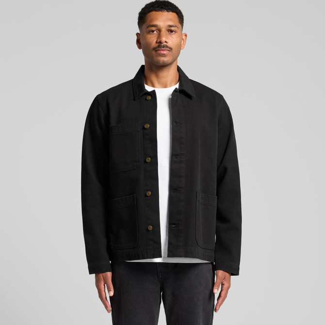 A man wearing a black canvas chore jacket with button closure and multiple pockets. The background is plain grey.