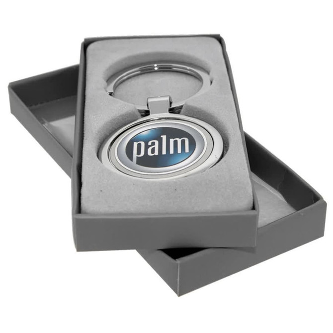 A silver keychain with a circular emblem in a grey box with a soft interior. The keychain includes a logo.