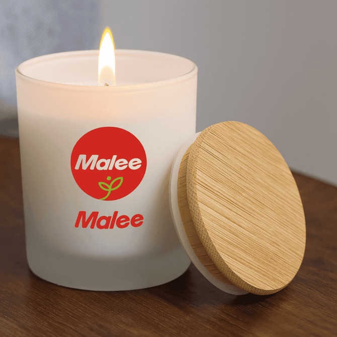 A small white candle with a wood lid, featuring a logo, and a lit flame on a wooden surface.