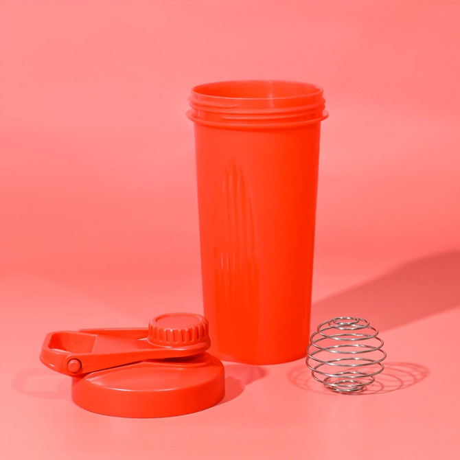A drink bottle in vibrant red with a screw-on lid and a metal whisk ball for mixing. It features a logo on the side.