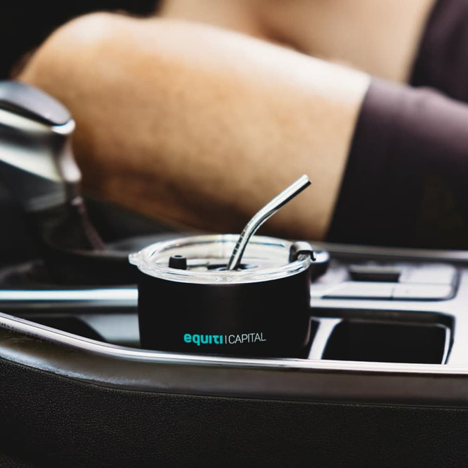 A drink bottle featuring a black design, with a metal straw, placed in a car cup holder. Includes a logo.