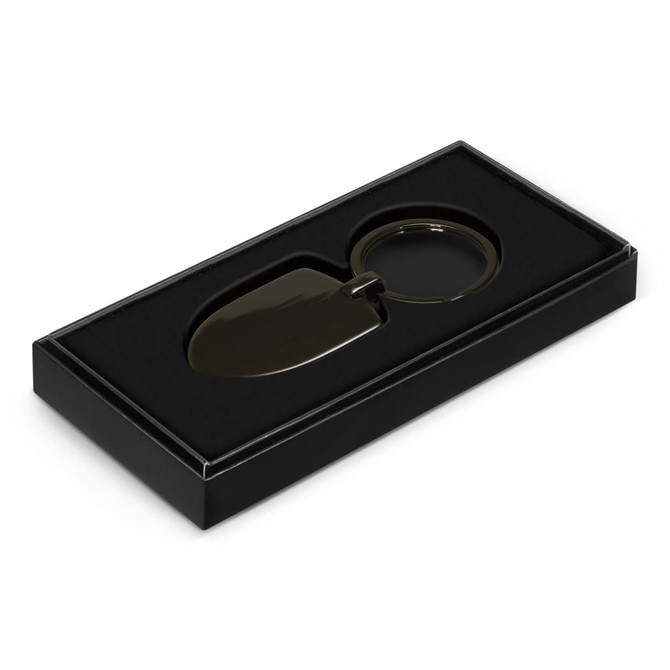 A black gift box containing a green shovel-shaped key ring with a circular attachment.