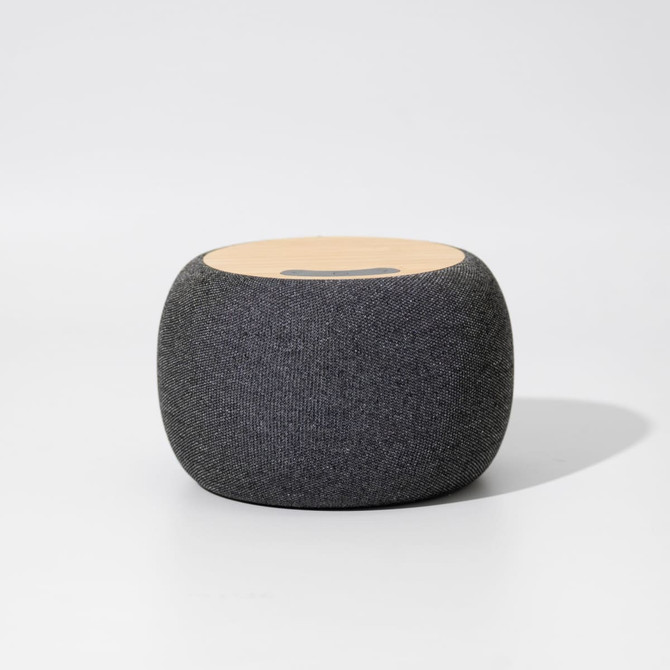 A round, grey wireless speaker with a wooden top surface and a logo on it.