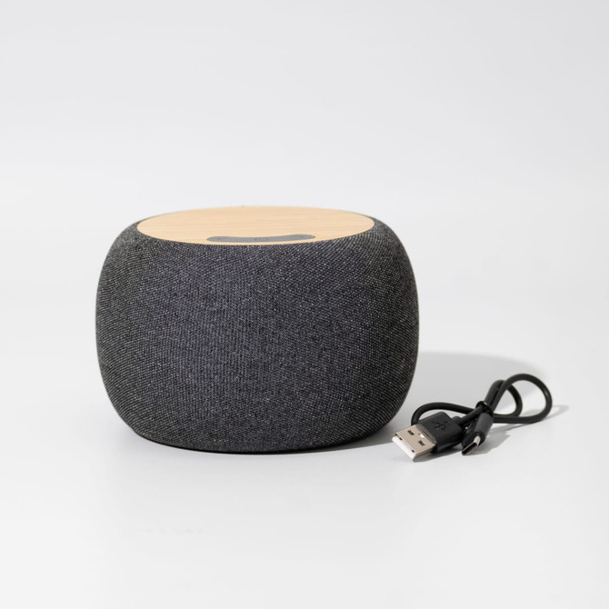 A round, grey wireless speaker with a wooden top and a USB cable beside it.